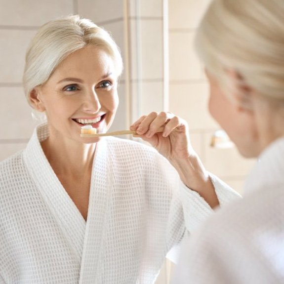 a woman smiling while brushing her teeth