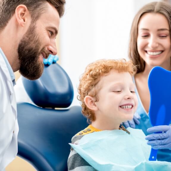 Children's dentist team member and young dental patient smiling during dental checkup and teeth cleaning for kids