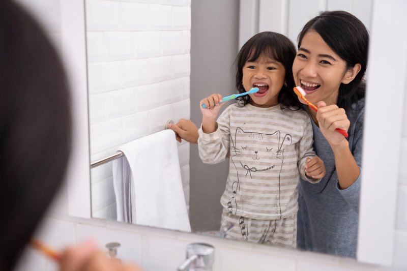 a girl and her mother brushing their teeth 